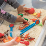 Kids playing in a sensory bin filled with rice and small toys as part of an occupational therapy activity for tactile defensiveness.