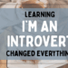 A woman with a cup of cocoa reading a book with a leaf on top of it with the title Learning I’m an Introvert Changed Everything overlaid.
