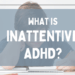 A young person sits at a desk, head resting on one hand while writing with a pencil, appearing distracted or fatigued. A semi-transparent blue banner overlays the image with the text 'What Is Inattentive ADHD?' in bold white lettering.
